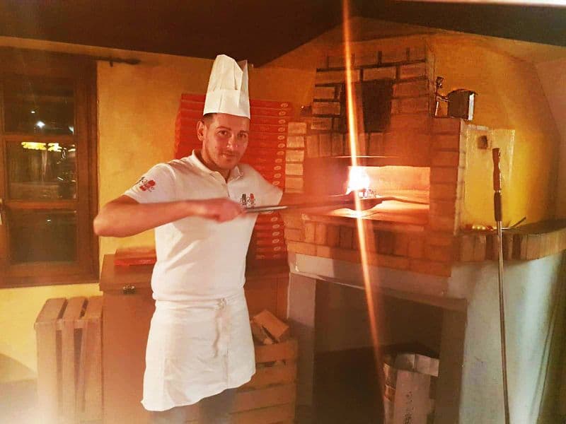 Pizzaiolo schiebt eine Pizza mit dem Holzofenschieber ins Feuer
