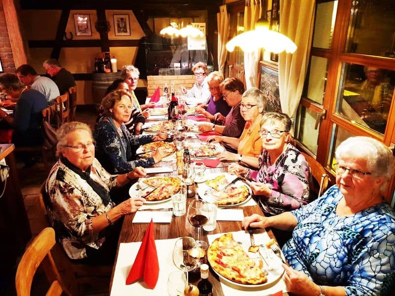 Grössere Gästerunde isst gemeinsam Pizza am langen Tisch