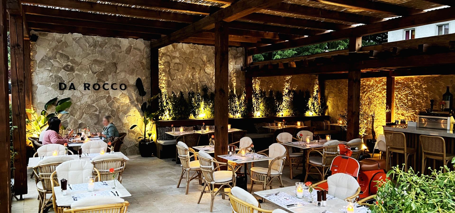 Terrasse am Abend mit dem Schriftzug DA ROCCO auf der Natursteinwand